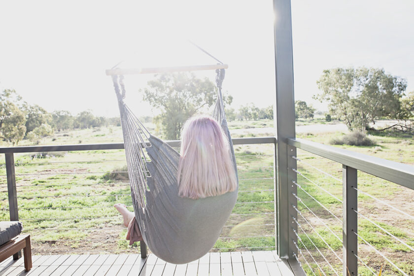 Lady sits in hanging chair at luxury accommodation.