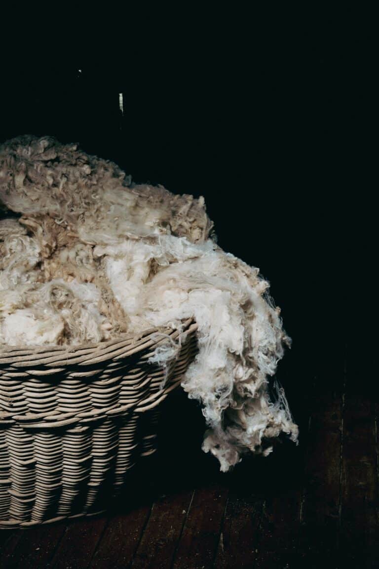 Raw wool fleece overflows from woven basket against dark background.